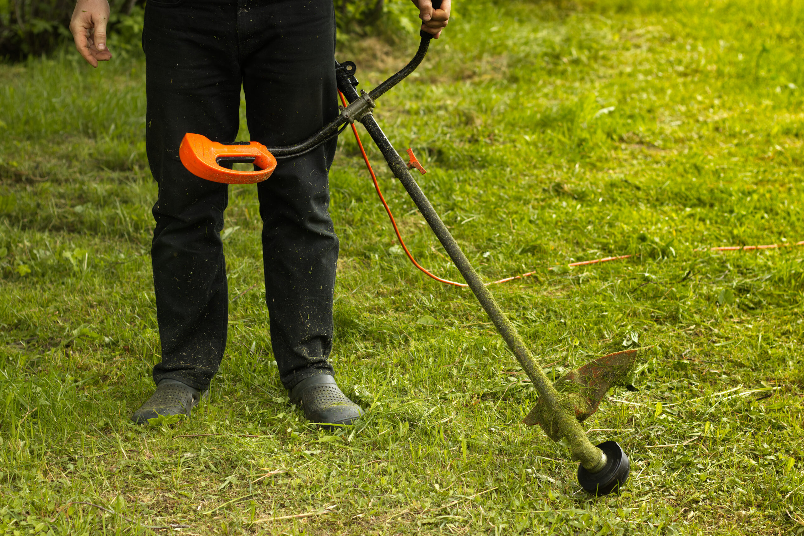Man Holding A String Trimmer And Cutting Grass In A Garden
